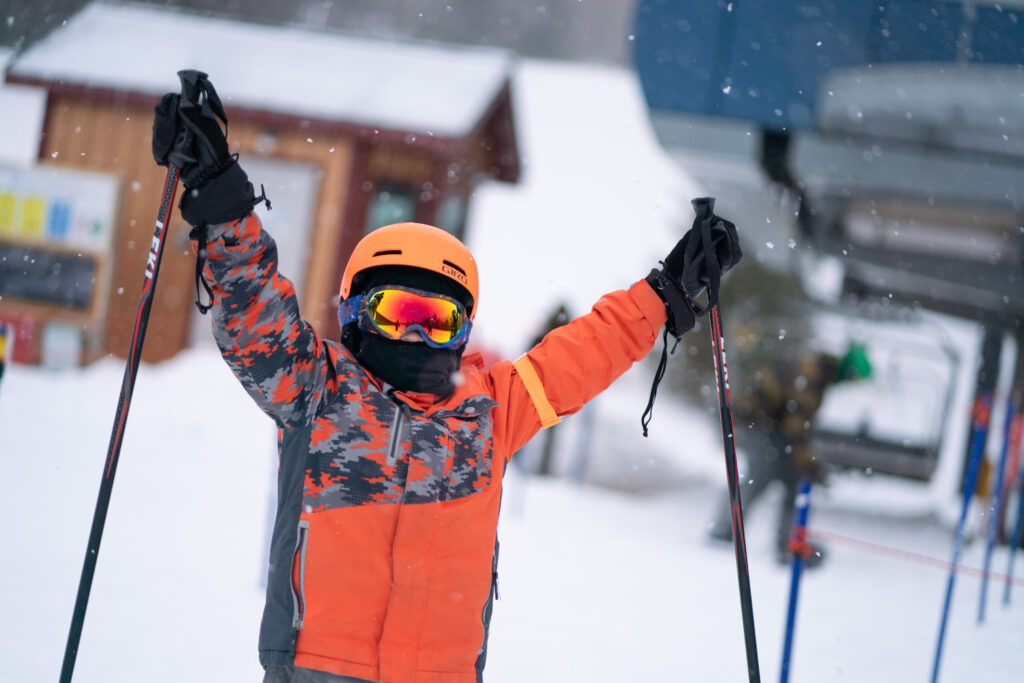 Kid in orange raising hands while skiing